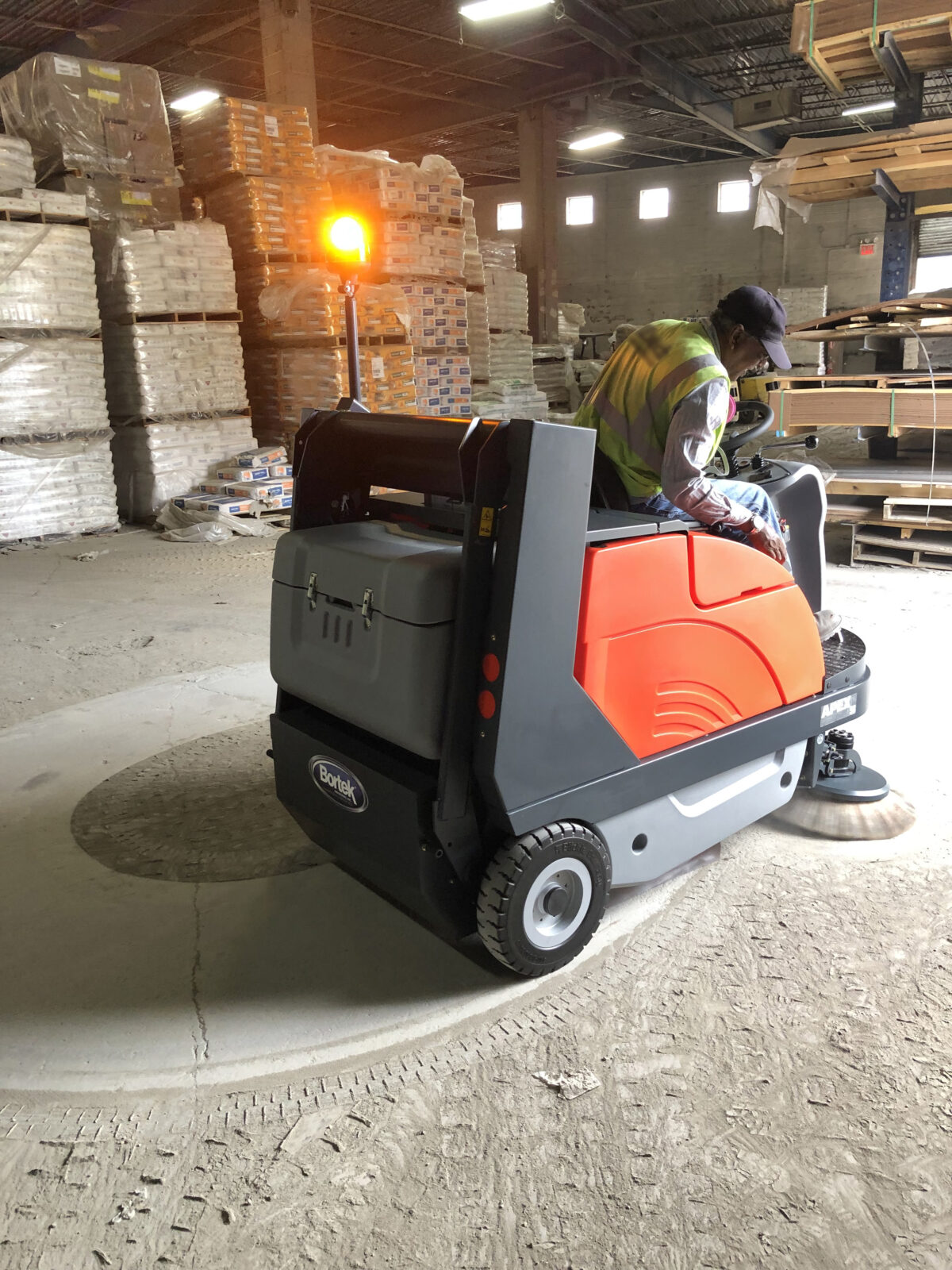 PowerBoss Apex 58 Rider Sweeper cleaning dust from a warehouse floor