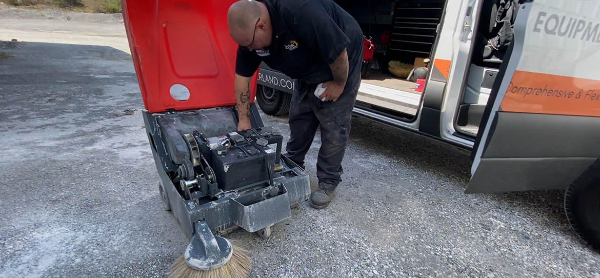 Technician repairing a walk-behind sweeper next to a service van